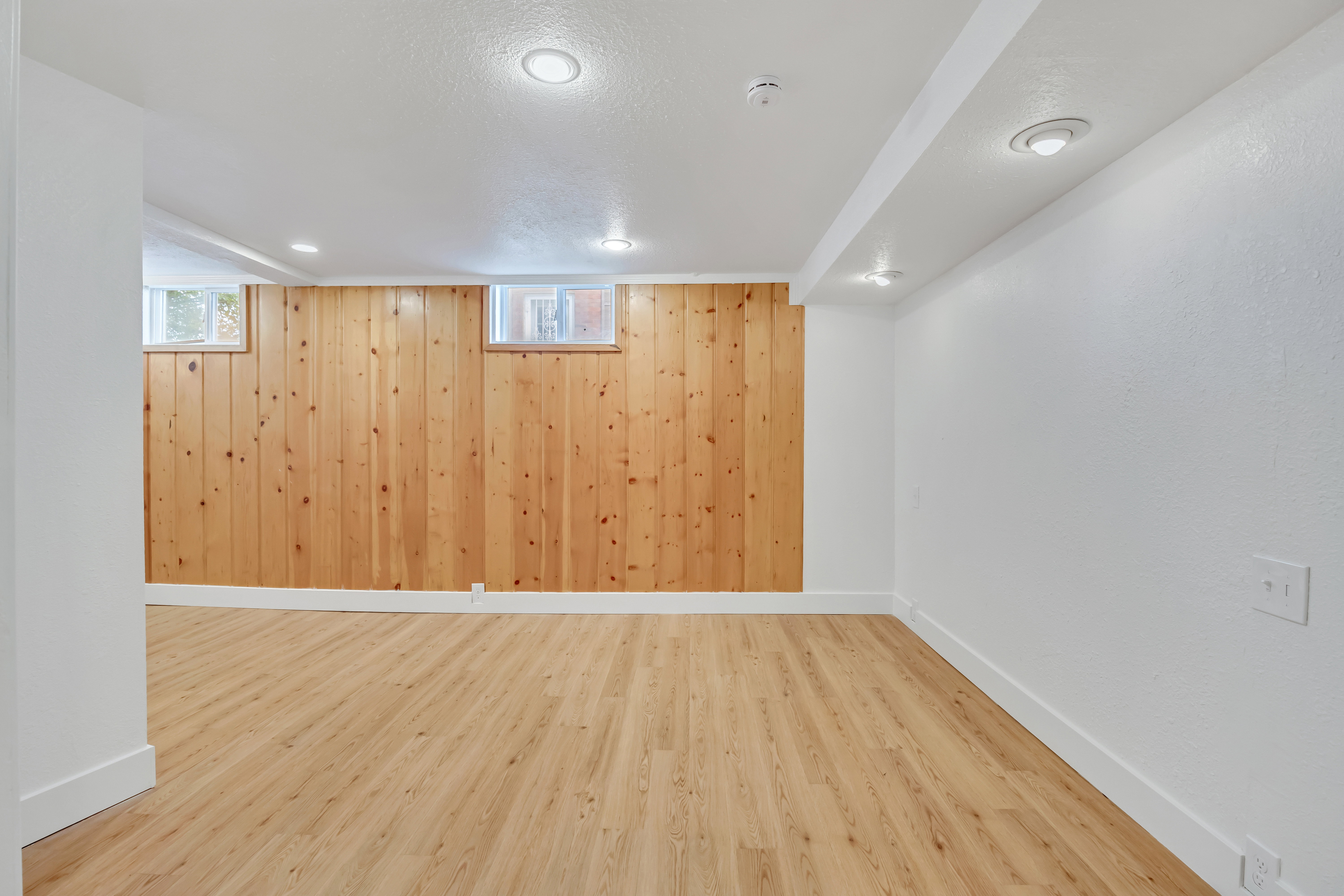 Finished lower level space featuring wood-finish flooring, recessed ceiling lighting, and natural wood paneling