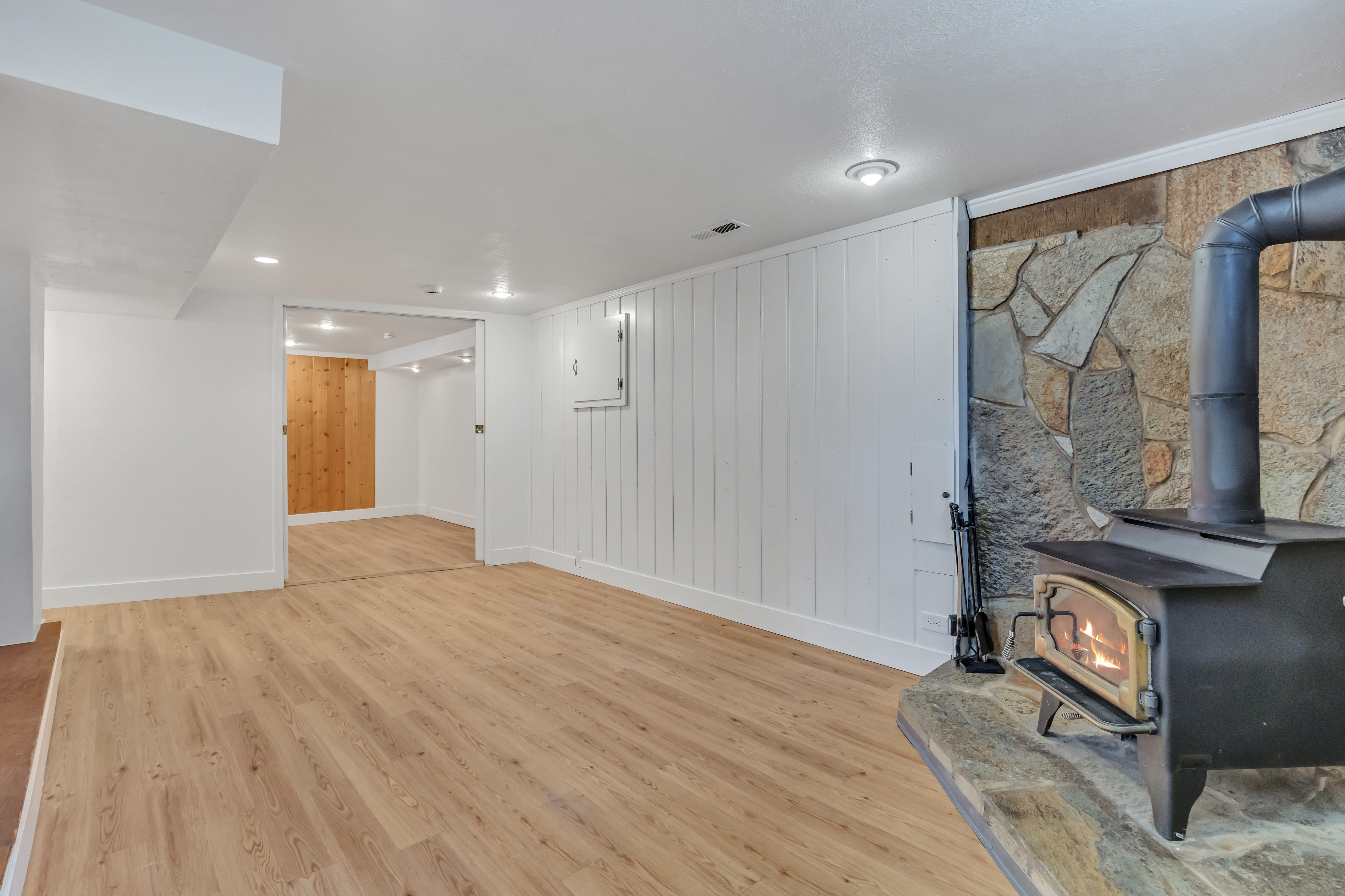 Living area featuring a stone accent wall, a wood-burning stove with a stone hearth, wood-finish flooring, and recessed lighting