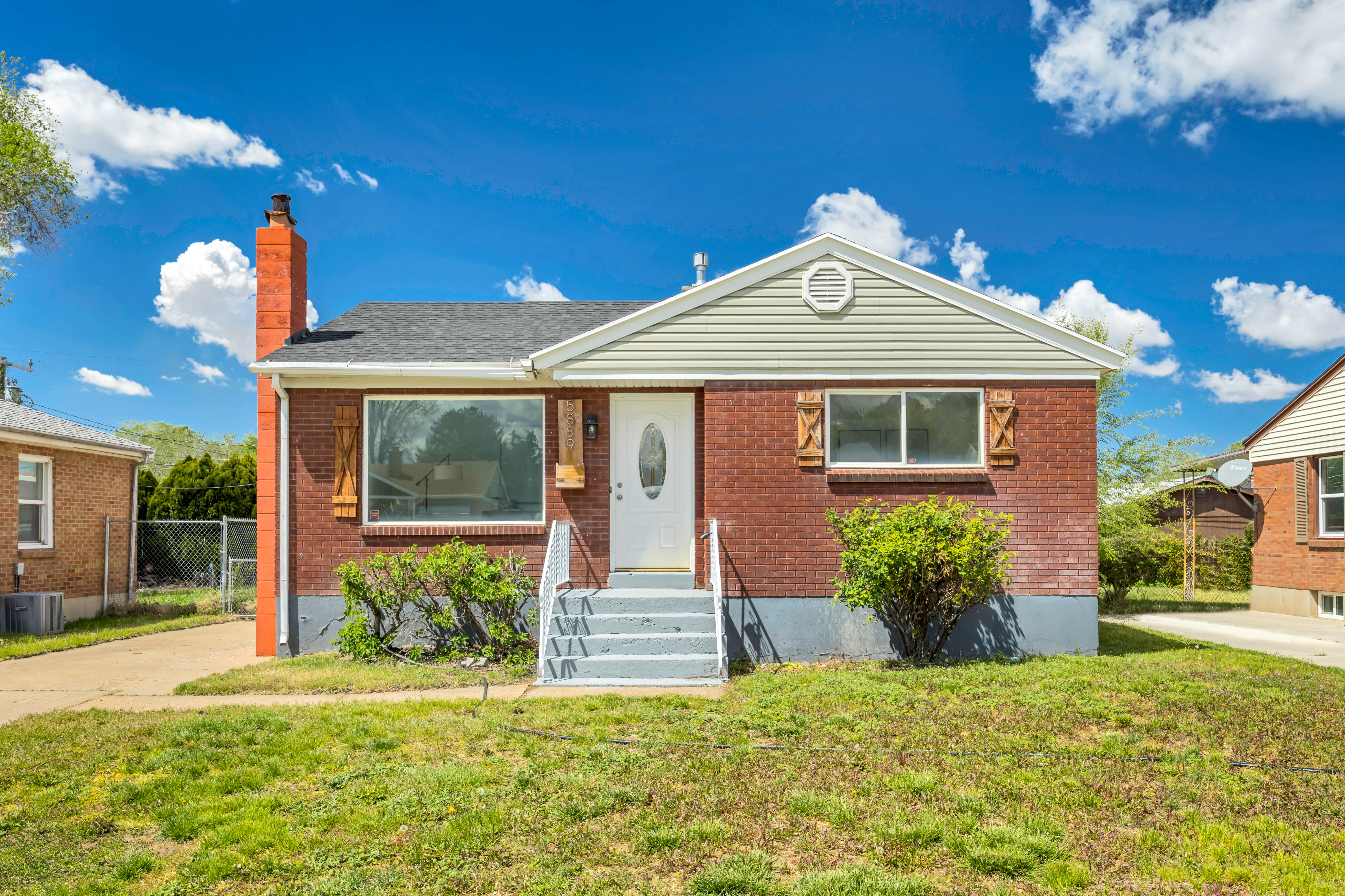 Brick exterior with a prominent chimney, featuring a white oval-lite entry door and light blue painted steps