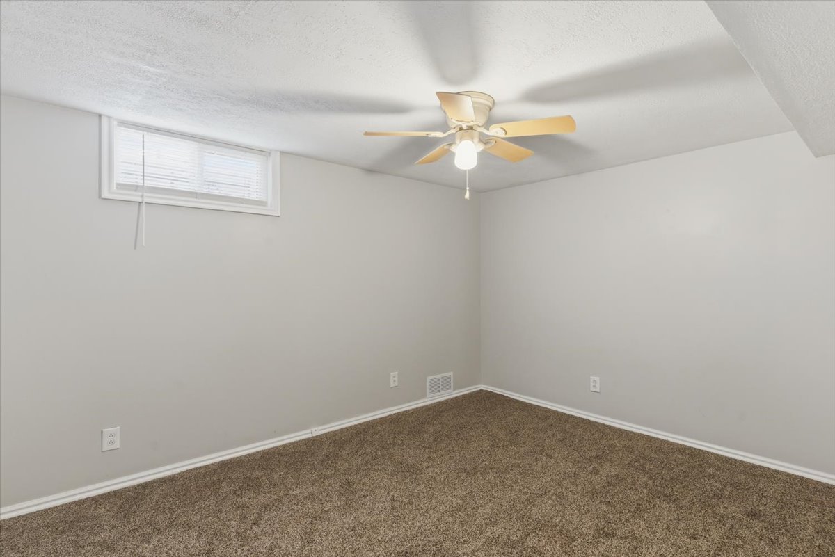 Room featuring neutral tone walls, brown carpeting, and a ceiling fan with light fixture