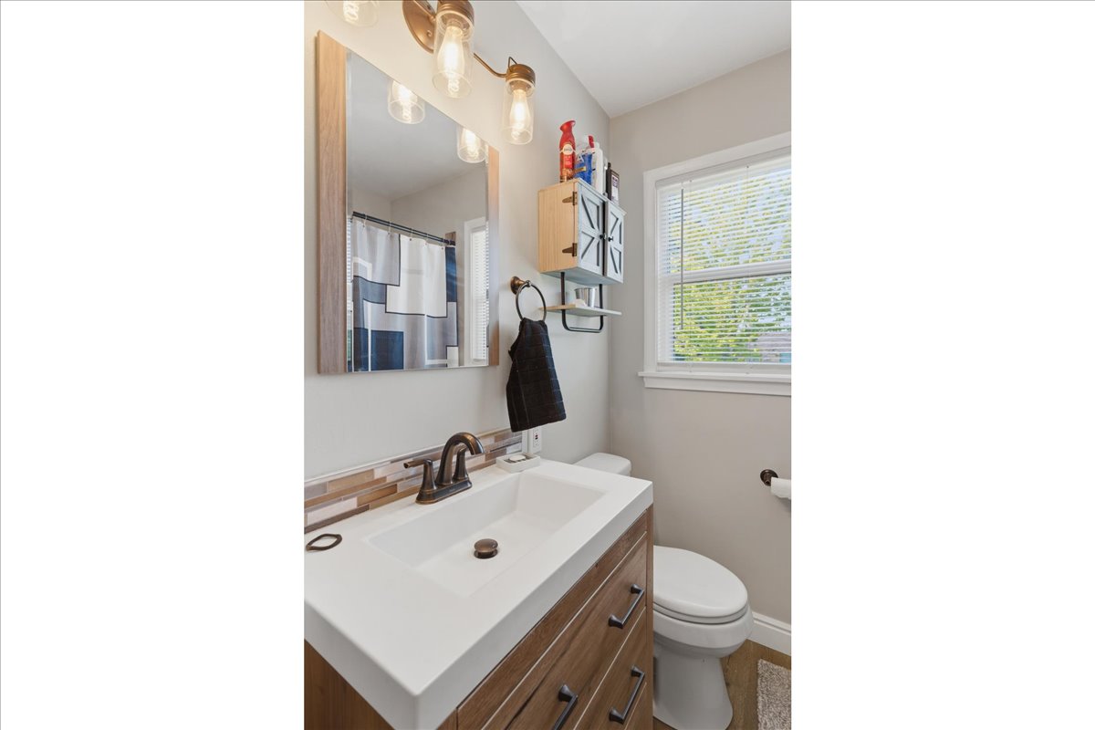 Bathroom featuring a wood-finish vanity with a white rectangular sink, bronze faucet, and a multi-toned tile backsplash