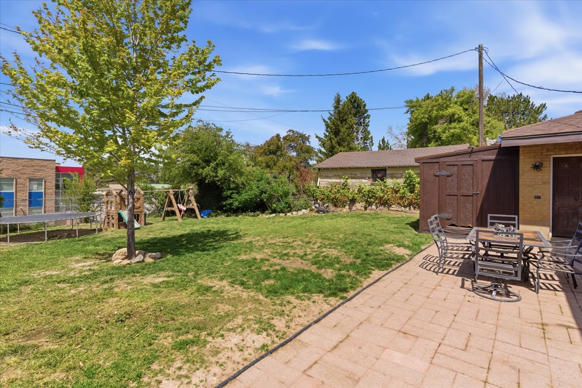 Expansive backyard featuring a paver patio, a freestanding storage shed, and mature trees