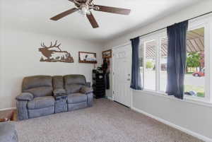 Living space featuring light-toned carpeting, a ceiling fan with wood-finish blades, and white walls