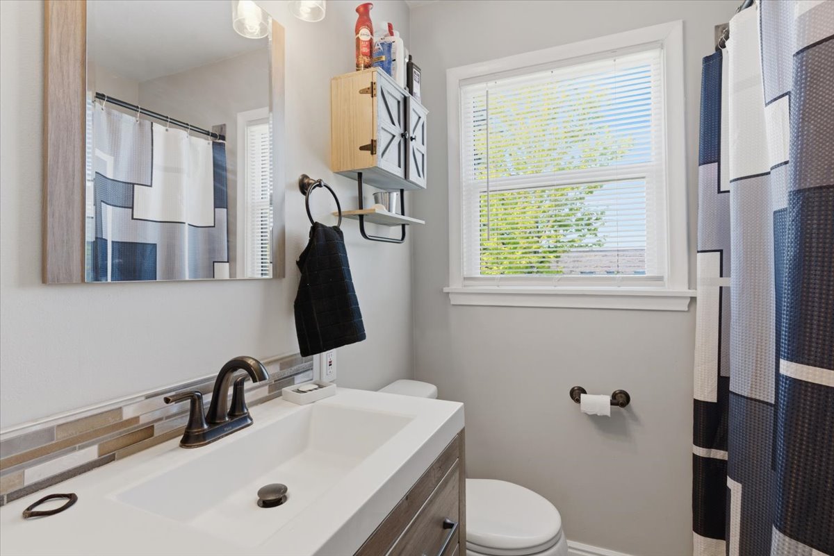 Contemporary bathroom featuring a single white basin, dark bronze faucet, and a mosaic tile backsplash