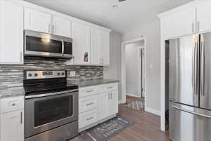 Contemporary kitchen featuring white shaker cabinetry, stainless steel appliances, granite-style countertops, mosaic tile backsplash, and wood-finish flooring