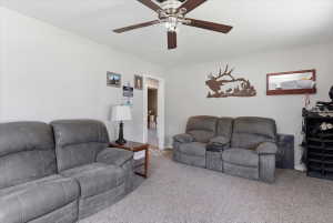 Living area featuring carpet flooring, light-toned walls, and a ceiling fan with wood-finish blades