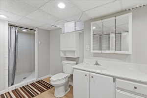 Bathroom featuring a walk-in shower with white tile surround, a white vanity with an integrated sink and white countertop, a tri-fold mirrored medicine cabinet, a toilet, and wood-finish flooring