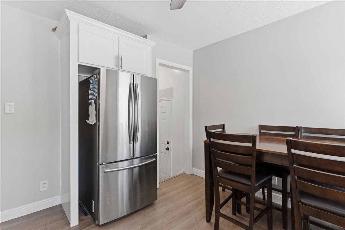Stainless steel refrigerator integrated with custom white upper cabinetry, wood-finish flooring, and a dark wood dining set