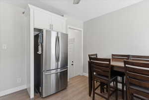 Stainless steel refrigerator integrated with custom white upper cabinetry, wood-finish flooring, and a dark wood dining set