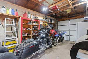 Garage interior featuring a sectional garage door, exposed wood rafters, concrete block walls, and built-in shelving