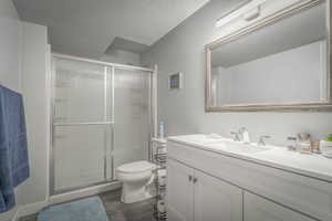 Bathroom with vanity, a stall shower, a textured ceiling, and dark wood-style floors