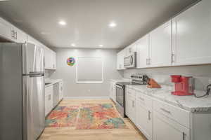 Kitchen with stainless steel appliances, white cabinets, light wood finished floors, and recessed lighting