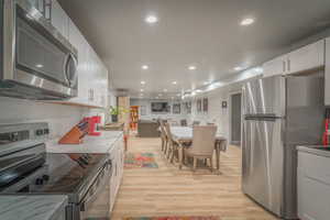 Kitchen with stainless steel appliances, recessed lighting, white cabinets, open floor plan, and light countertops