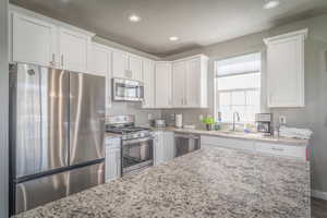 Kitchen featuring stainless steel appliances, recessed lighting, white cabinets, and light stone counters
