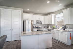 Kitchen featuring stainless steel appliances, white cabinetry, dark wood-type flooring, recessed lighting, and light stone counters