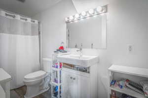 Bathroom featuring a white vanity with an integrated sink, a wall-mounted mirror with vanity lighting, and a commode