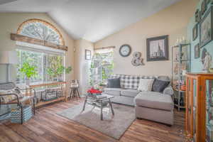 Spacious living area featuring high vaulted ceilings, wood-finish flooring, and ample natural light from multiple windows, including an arched transom window