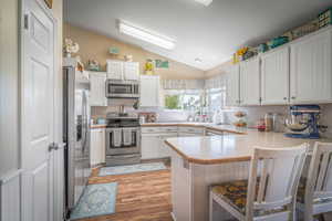 Spacious kitchen featuring white cabinetry, stainless steel appliances, wood-finish flooring, and a breakfast bar island
