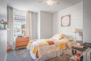 Carpeted room featuring a ceiling fan with integrated lighting, a window with an arched transom, and a shiplap accent wall
