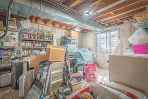 Exposed ceiling joists with visible ductwork and wiring, concrete walls, and a small window present in a utility space