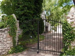 Wrought iron driveway gate flanked by stone pillars with mature ivy