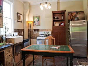 Kitchen featuring a white farmhouse sink, pressed tin backsplash, stainless steel refrigerator, and a tiled countertop dining table