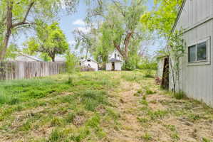 Expansive rear yard with mature perimeter trees, a wooden privacy fence, and a distant garage
