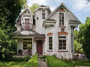 Ornate Victorian-style exterior featuring a prominent turret with fish-scale shingle siding, a second-story balcony with decorative railing, and a covered porch
