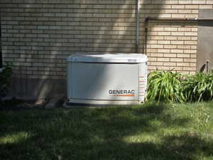 Generac whole-house generator on a concrete pad, positioned against a light brick exterior
