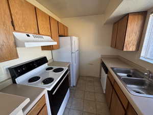 Kitchen featuring wood-finish cabinetry, a double-basin stainless steel sink, beige countertops, a white oven/range, and a white refrigerator