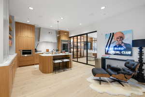 Open-concept kitchen featuring light wood-finish cabinetry, a large central island with seating, stainless steel appliances, and light wood-finish flooring
