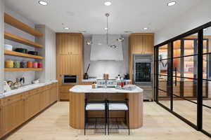 Modern kitchen featuring light wood-finish cabinetry, a central island with a white countertop, and integrated stainless steel appliances