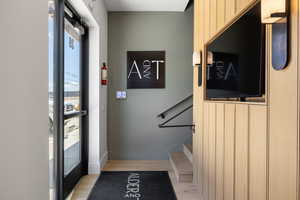 Entryway featuring vertical wood paneling, contemporary wall sconces, wood-finish flooring, and a black metal handrail leading to a lower level