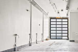 Interior commercial space featuring a full-light overhead door, exposed ceiling ductwork, and track lighting