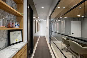 Hallway featuring a glass wall with black framing, wood-finish wall panels, recessed lighting, and a built-in storage unit with marble-finish countertop and light wood shelving