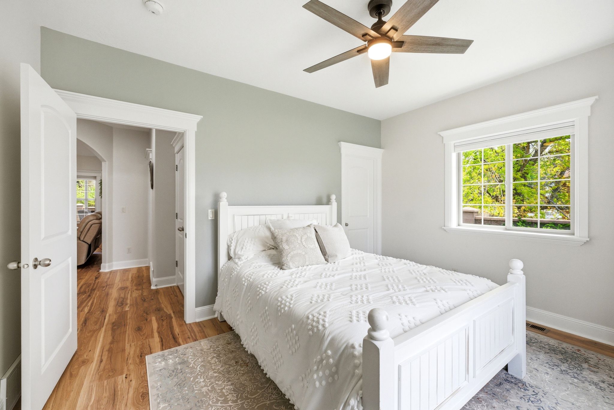 Bedroom with multiple windows, light wood-style floors, arched walkways, and a ceiling fan