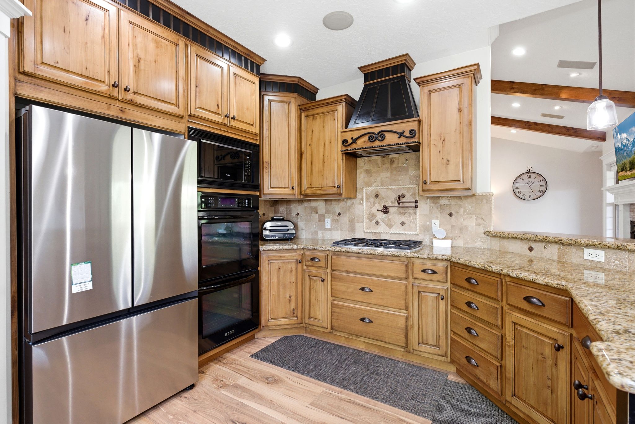 Kitchen featuring black appliances, light stone counters, tasteful backsplash, light wood-type flooring, and lofted ceiling with beams