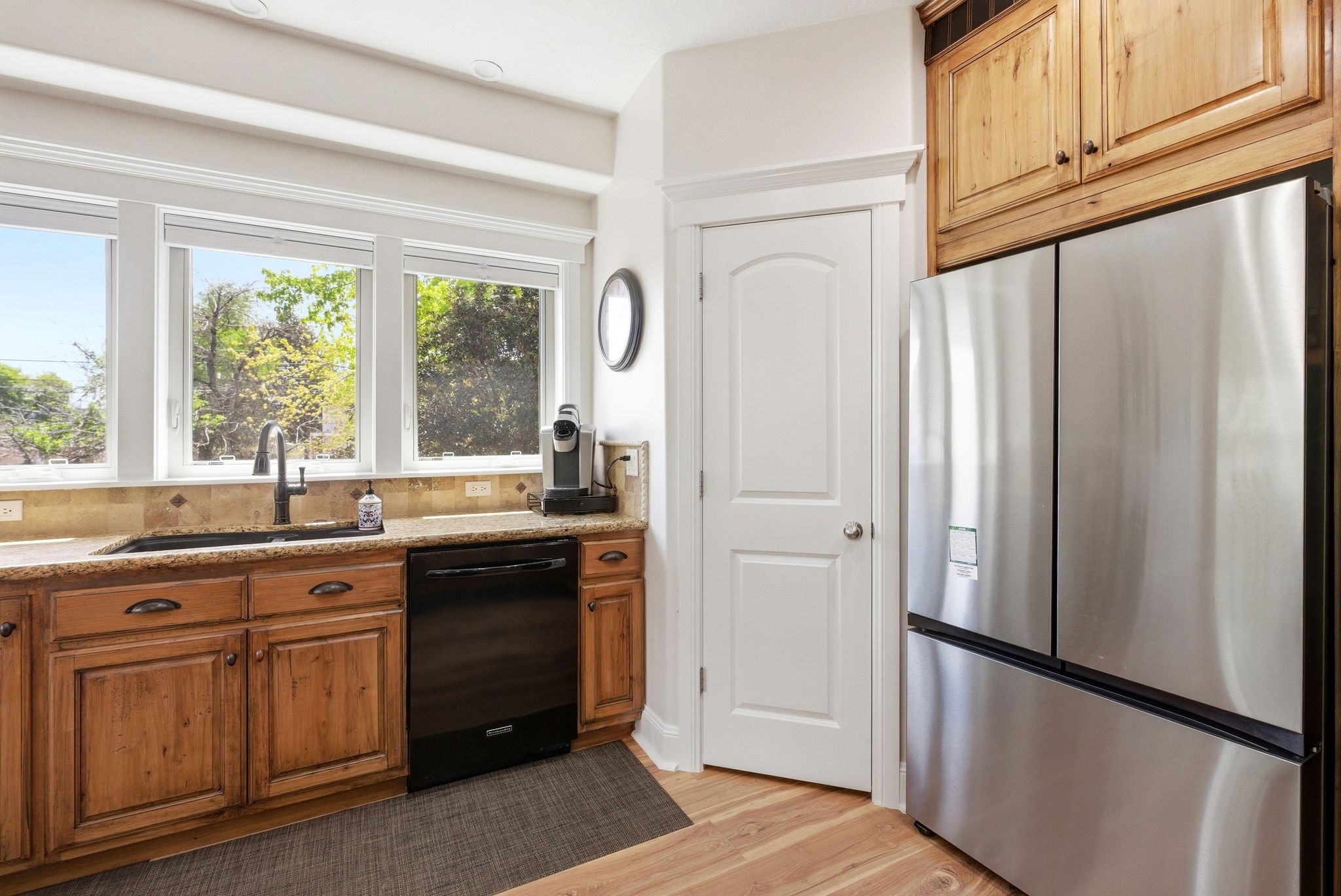 Kitchen with freestanding refrigerator, dishwasher, wood finish cabinets, light wood-type flooring, and light stone countertops