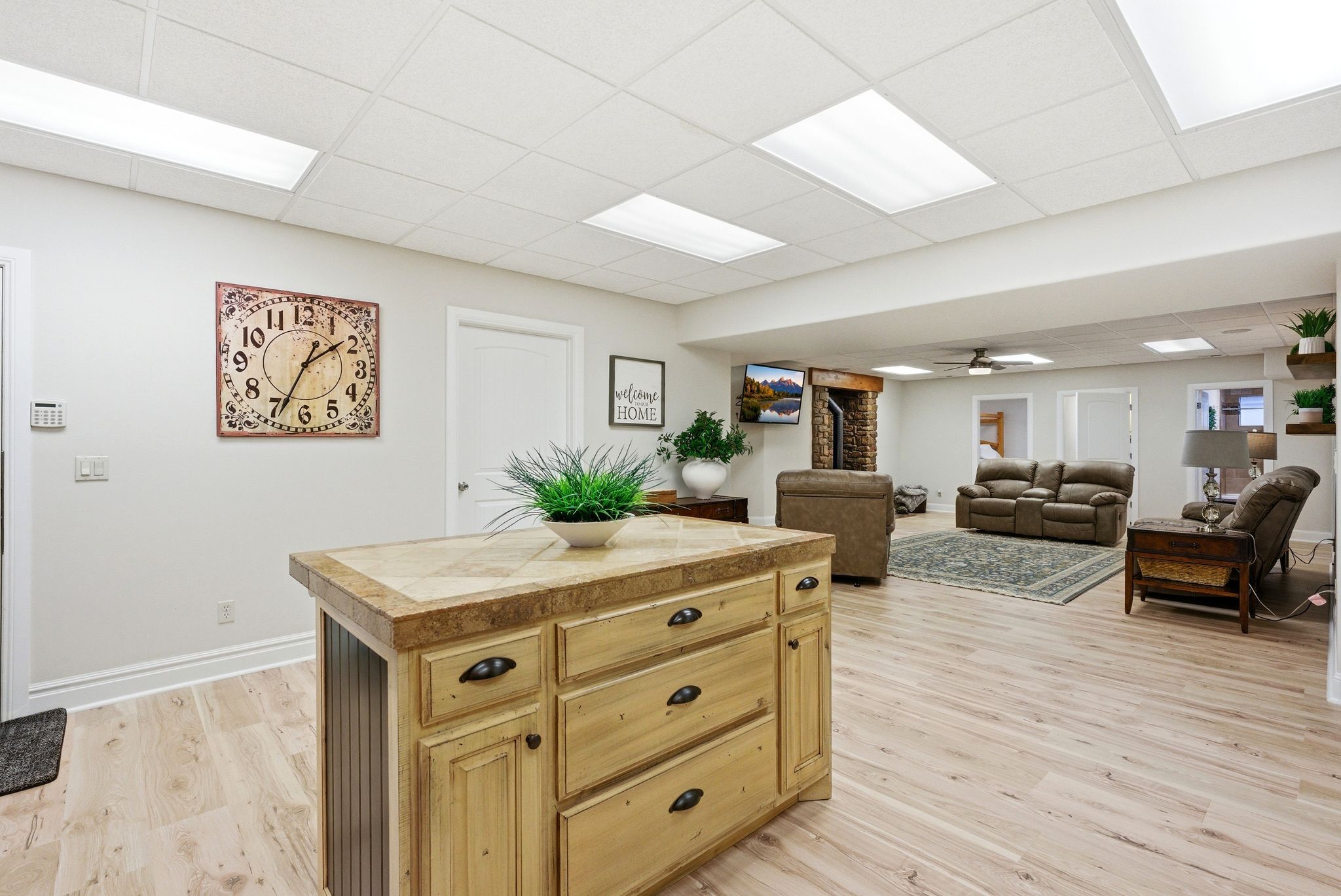 Kitchen featuring a paneled ceiling, open floor plan, ceiling fan, light wood-type flooring, and tile counters