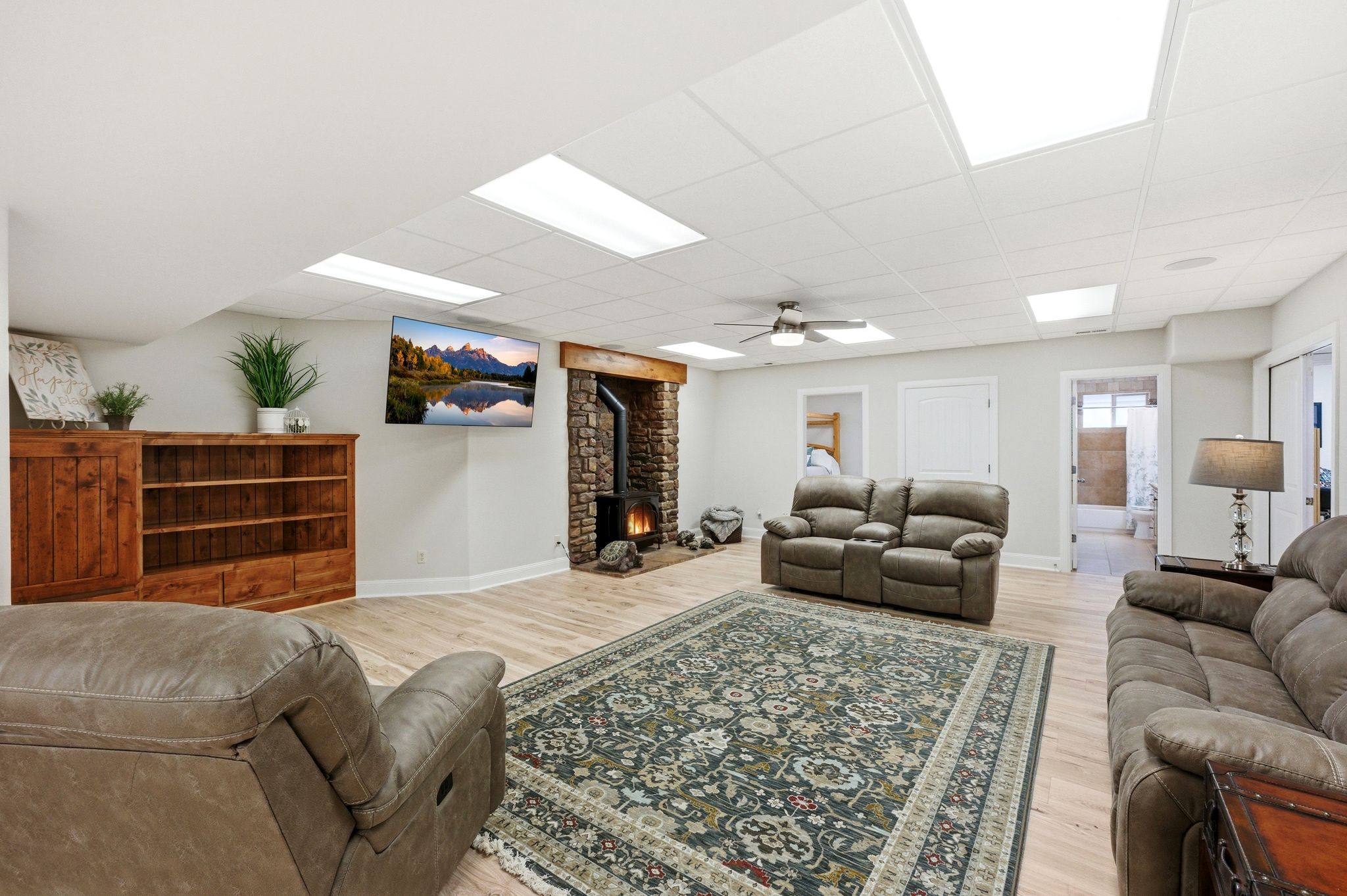 Living area featuring a wood stove, light wood-style floors, a drop ceiling, and ceiling fan