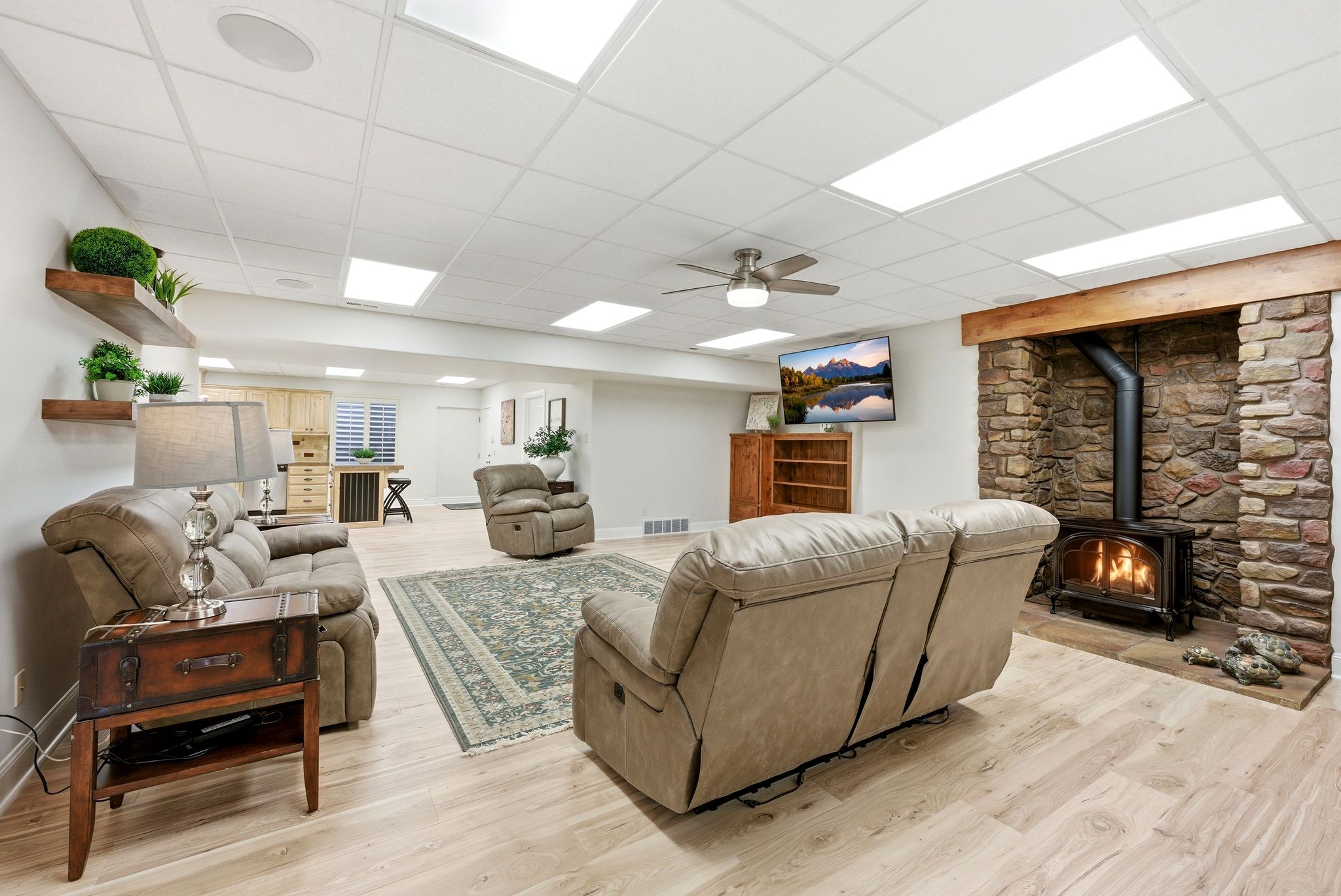 Living area with a wood stove, light wood-style flooring, a drop ceiling, and ceiling fan