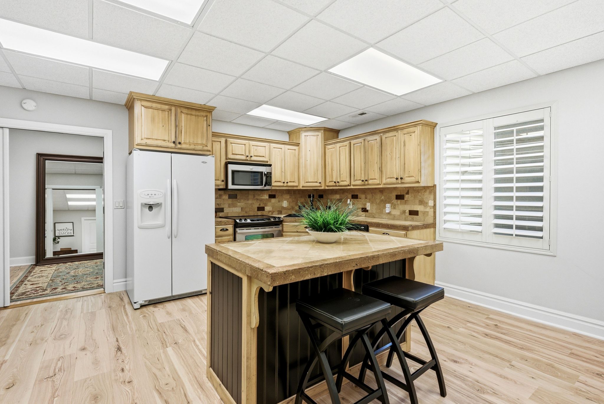 Kitchen with a kitchen bar, stainless steel appliances, light wood finish cabinetry, light wood-style floors, and a paneled ceiling