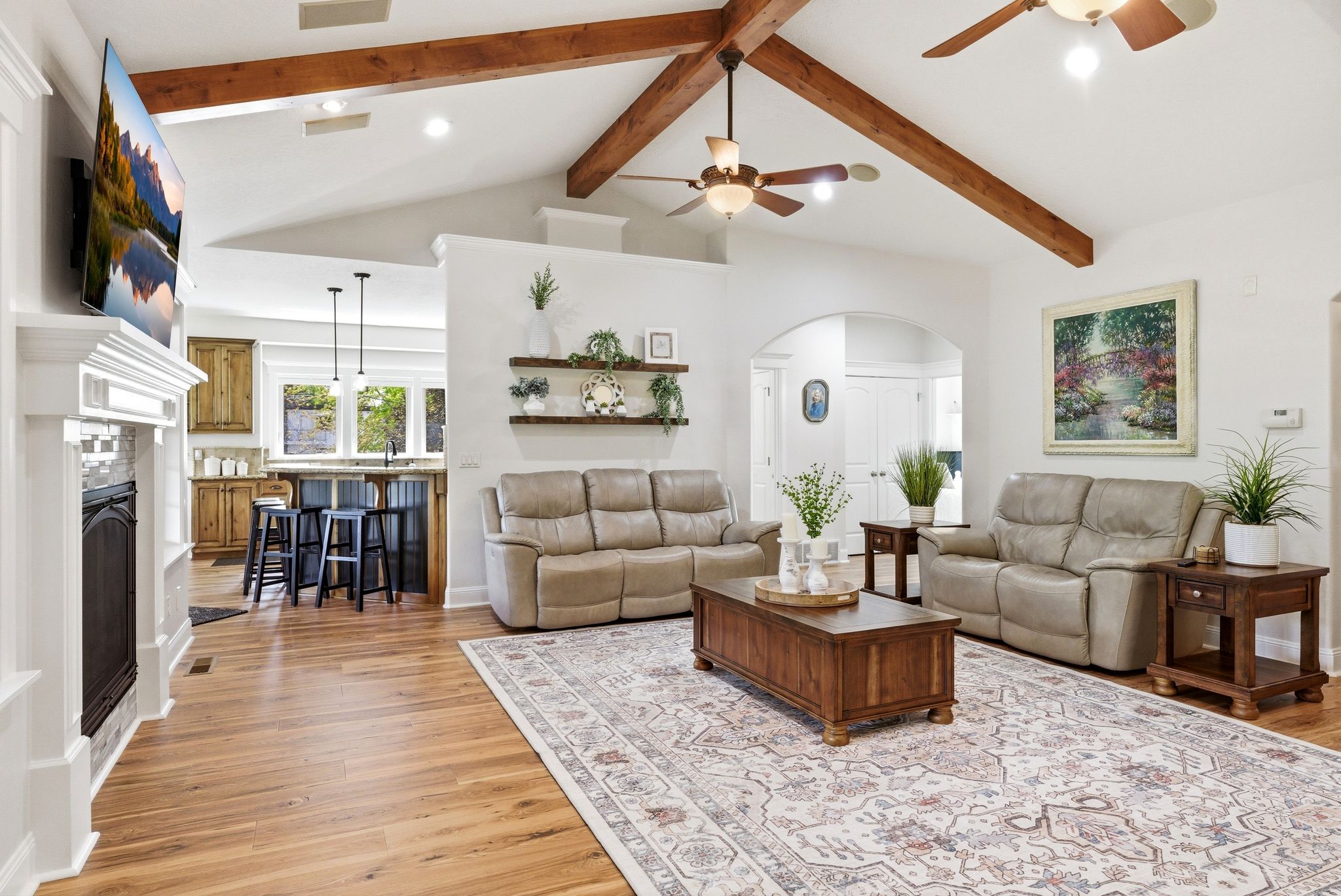 Living area with arched walkways, a ceiling fan, light wood finished floors, and a fireplace