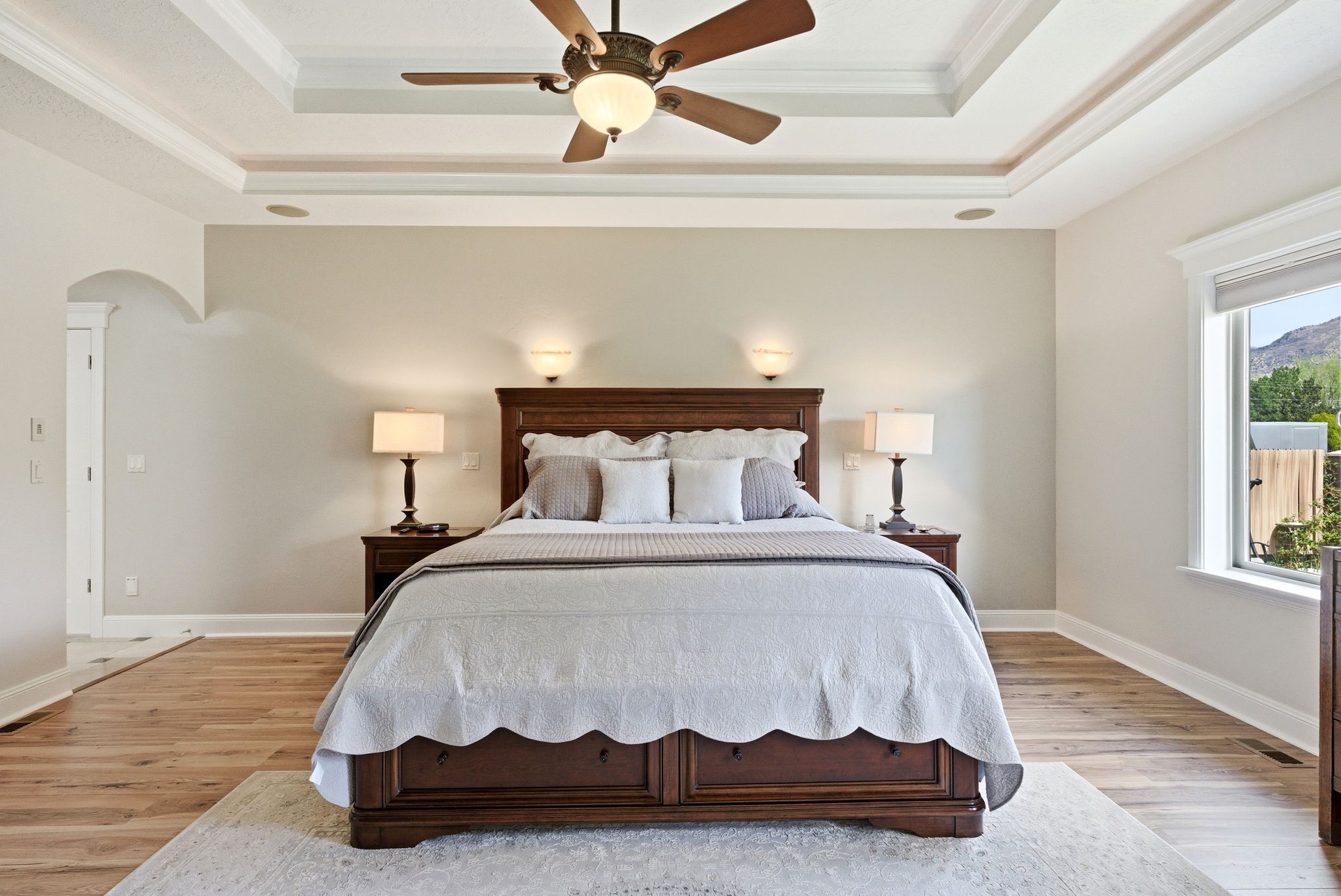 Bedroom with arched walkways, crown molding, light wood-style floors, ceiling fan, and a tray ceiling