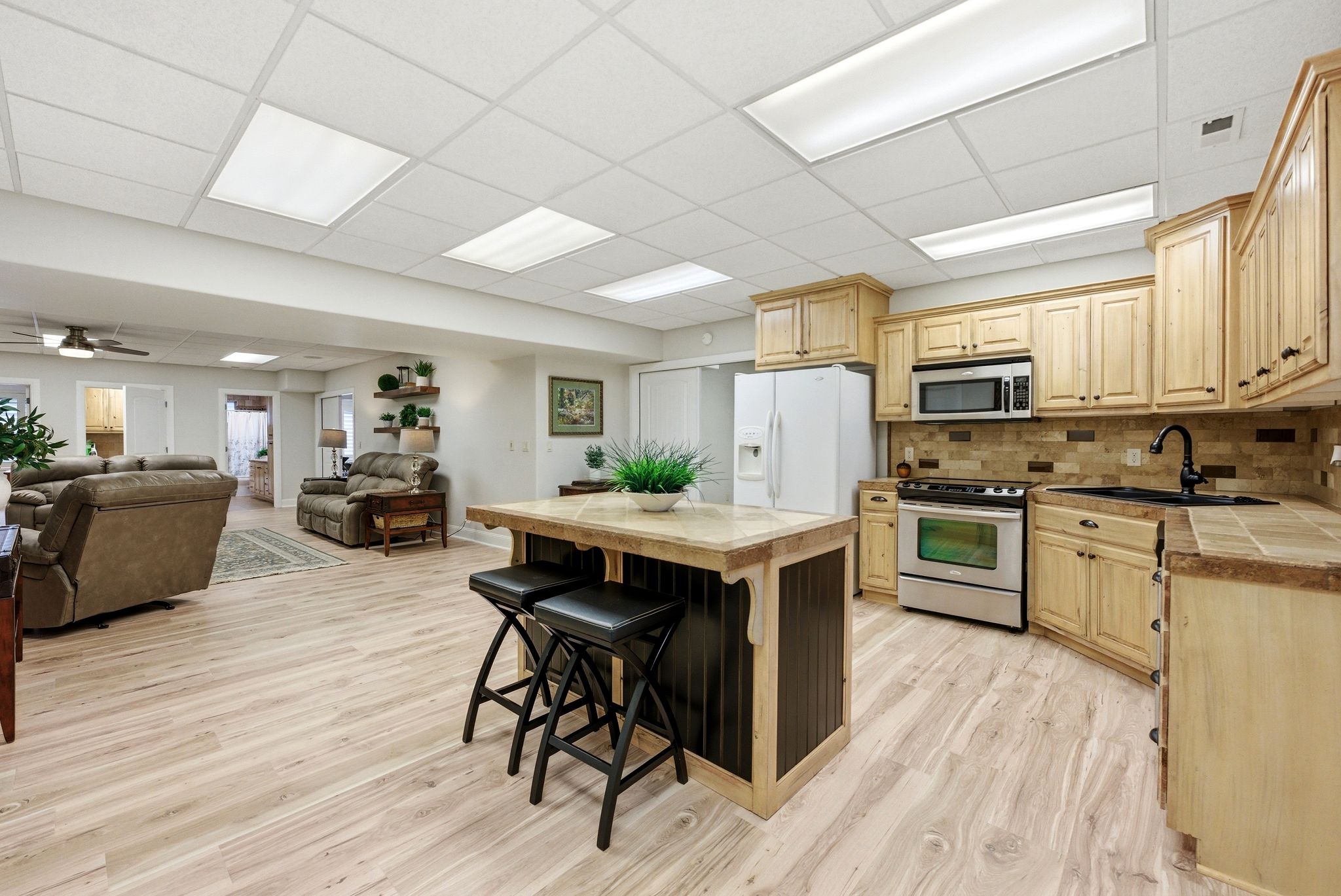 Kitchen featuring open floor plan, light wood finish cabinets, stainless steel appliances, a drop ceiling, and a kitchen breakfast bar