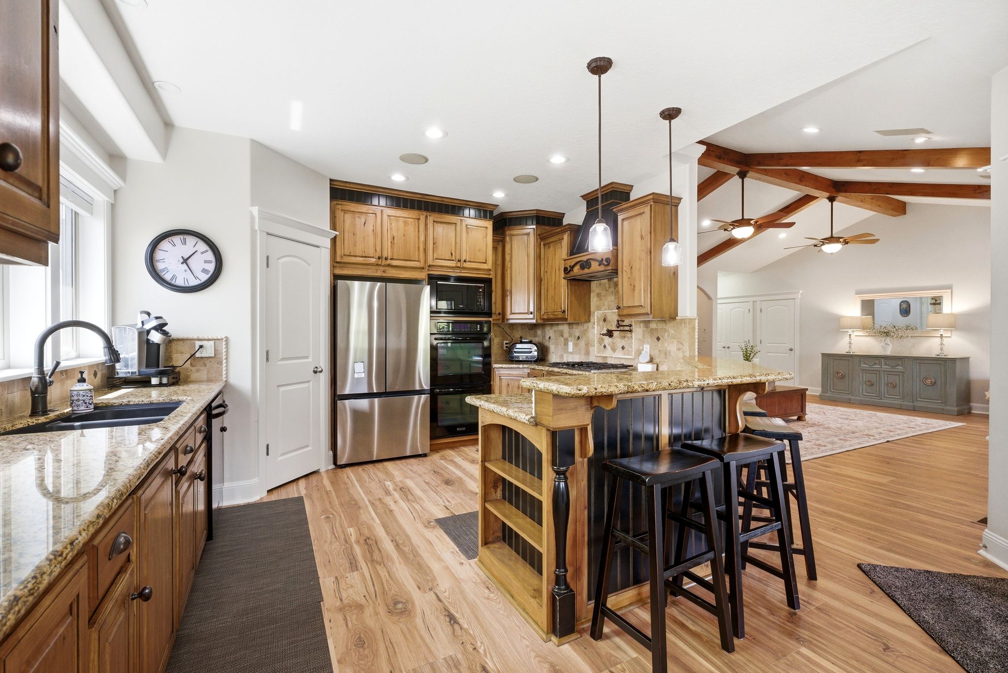 Kitchen featuring light stone countertops, a kitchen breakfast bar, black appliances, wood finish cabinets, and decorative backsplash