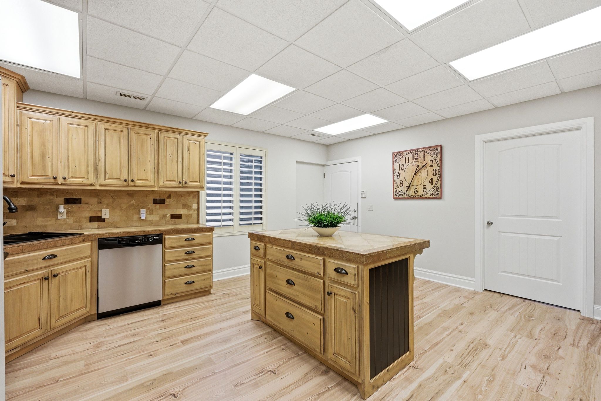 Kitchen with a kitchen island, tile counters, light wood-style flooring, decorative backsplash, and stainless steel dishwasher