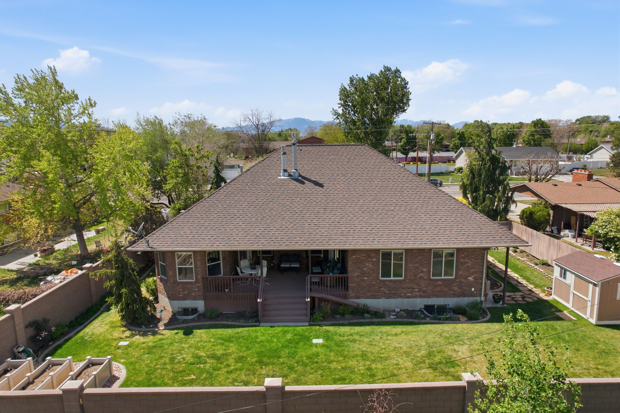 Back of house featuring a fenced backyard, roof with shingles, a wooden deck, a residential view, and brick siding