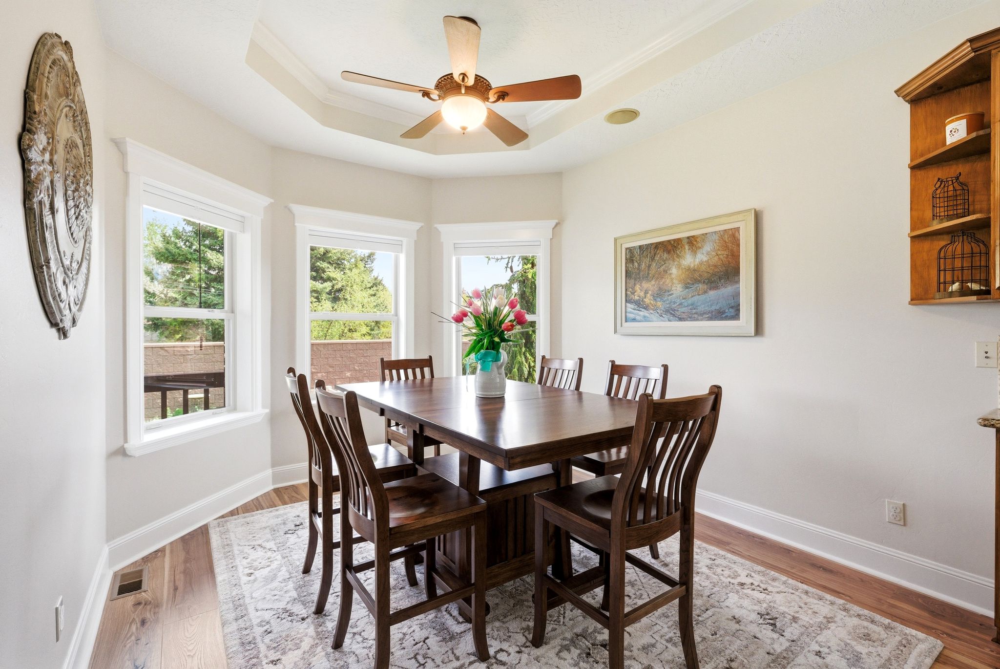 Dining area with light wood-style flooring, ceiling fan, ornamental molding, and a tray ceiling