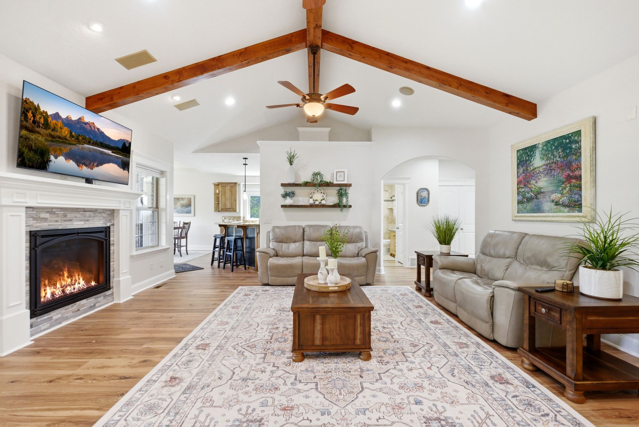 Living area with arched walkways, a ceiling fan, light wood-type flooring, a glass covered fireplace, and recessed lighting